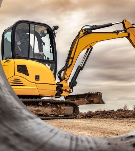 Mini excavator at the construction site on the edge of a pit against a cloudy blue sky. Compact construction equipment for earthworks. An indispensable assistant for earthworks